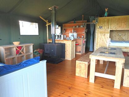 Experience the charm of a kitchen and dining area in a tent! This safari tent features a wood burning stove, a fully equipped kitchen, and a comfy cabin bed.